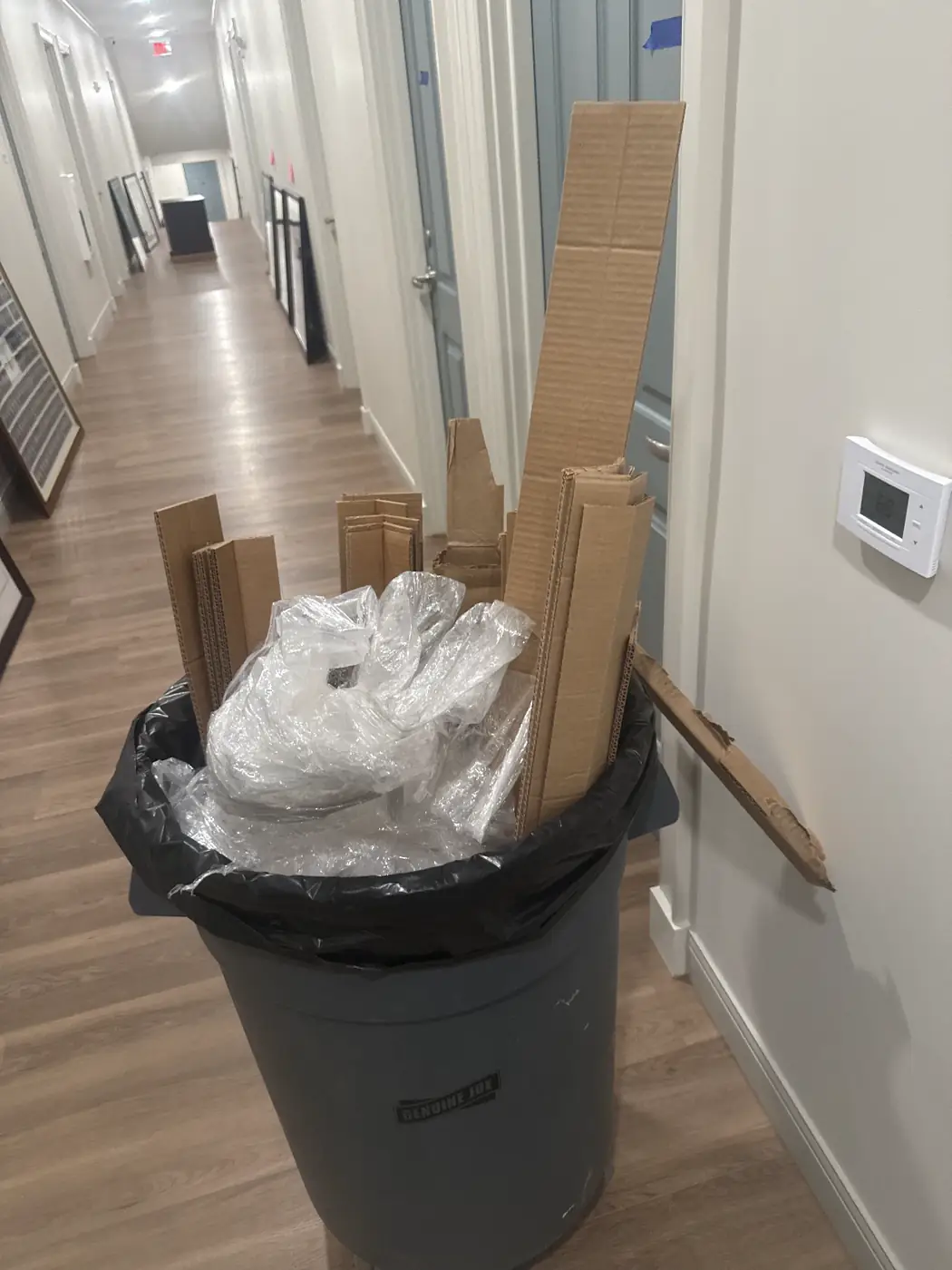 Trash can filled with cardboard and packing debris in an office hallway