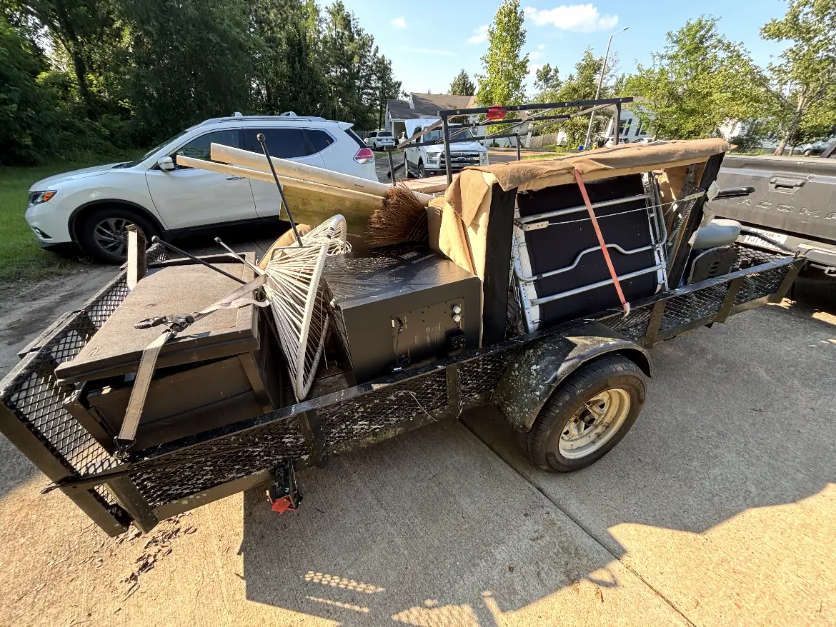 Trailer loaded with patio furniture, a rake, a broom, and a folding table